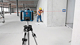 A Bosch Professional laser device is on a tripod, worker measures walls.