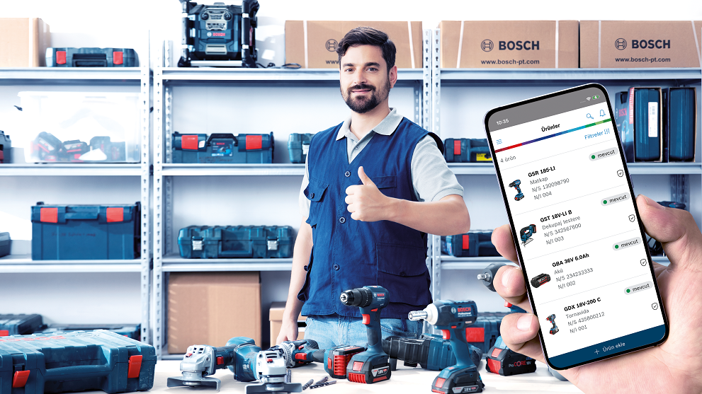 A man with a beard and blue vest gives a thumbs up in a room full of tools and boxes.