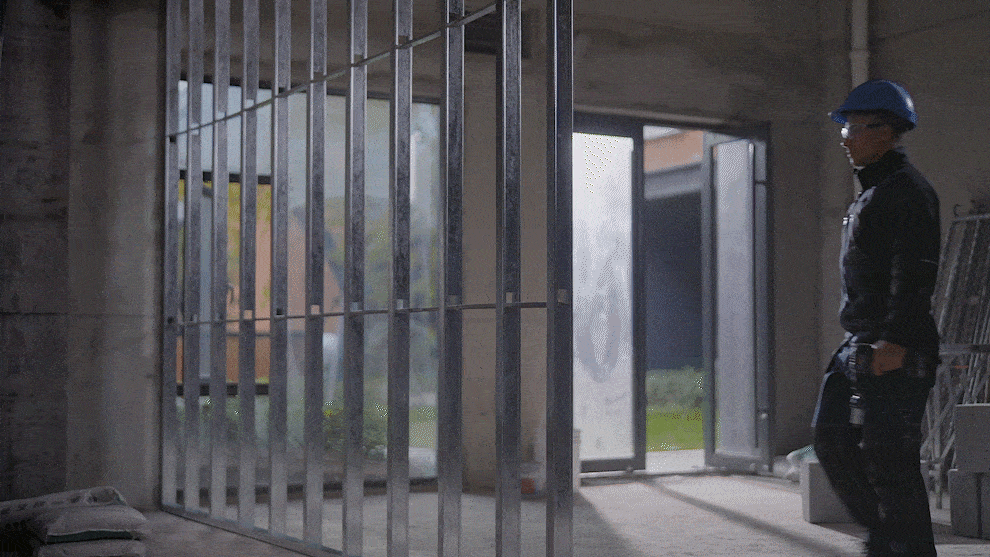 A worker with a blue helmet walks through a construction site with a metal frame.