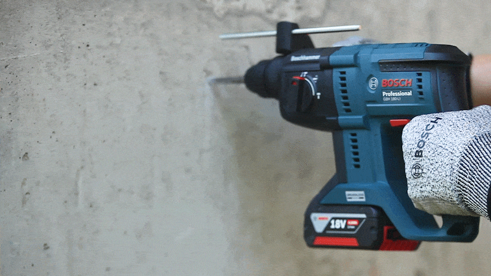 A Bosch Professional hammer drill is drilling into a gray concrete wall.