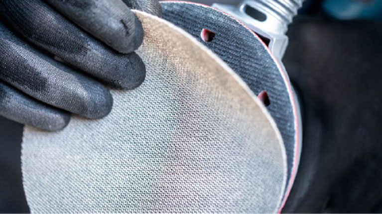 Two hands wearing black gloves hold a grinding disc.