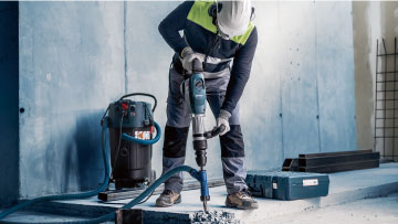 A worker with a helmet is drilling with a blue Bosch Professional tool.