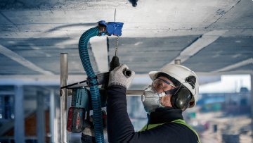 A craftsman with a helmet is drilling into a ceiling with a Bosch tool.