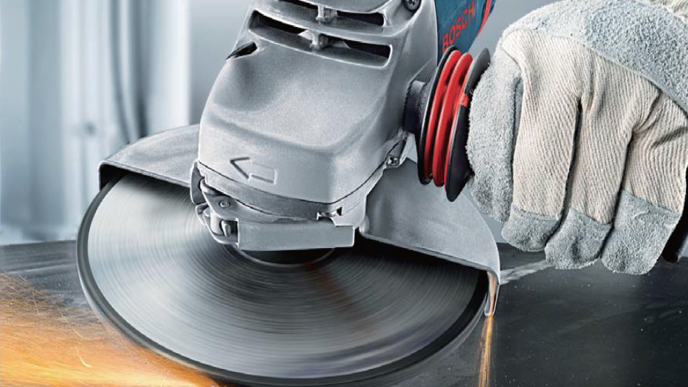 A hand with a gray Bosch Professional angle grinder is cutting metal.