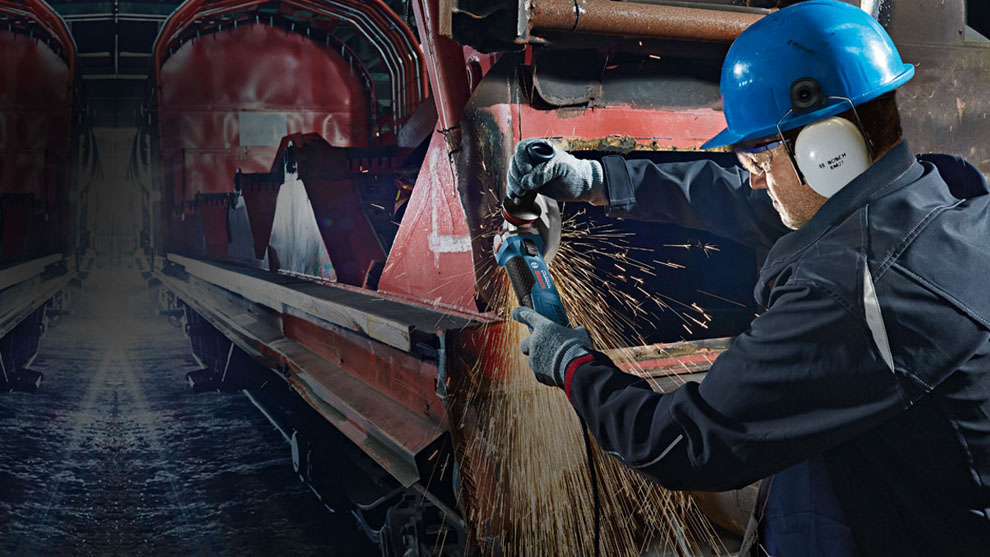 A man with a safety helmet is cutting metal, sparks are flying in the workshop.