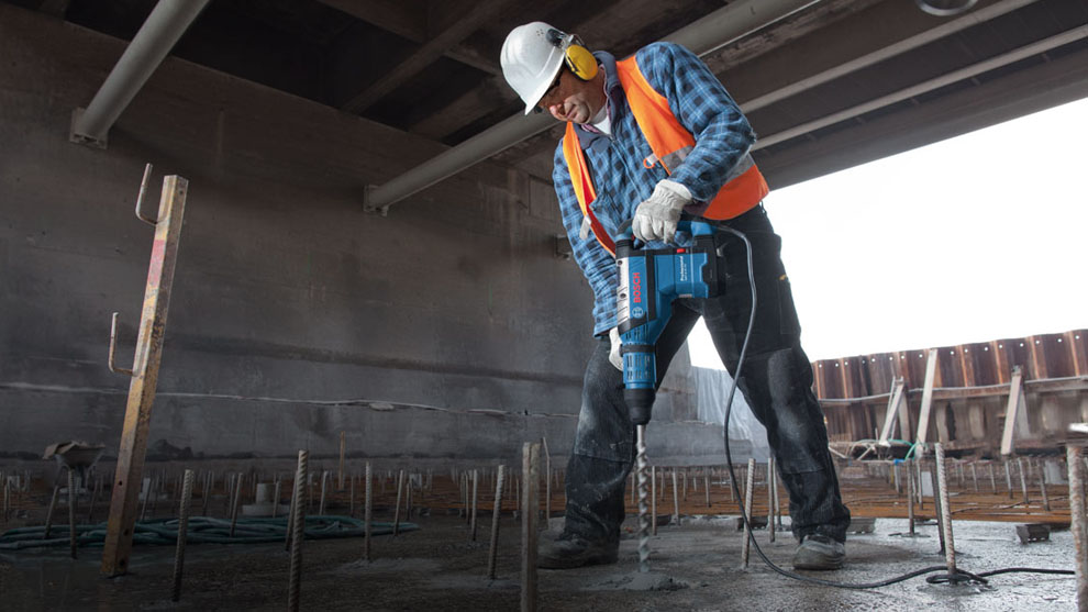 A worker with a jackhammer is working on a concrete floor at a construction site.