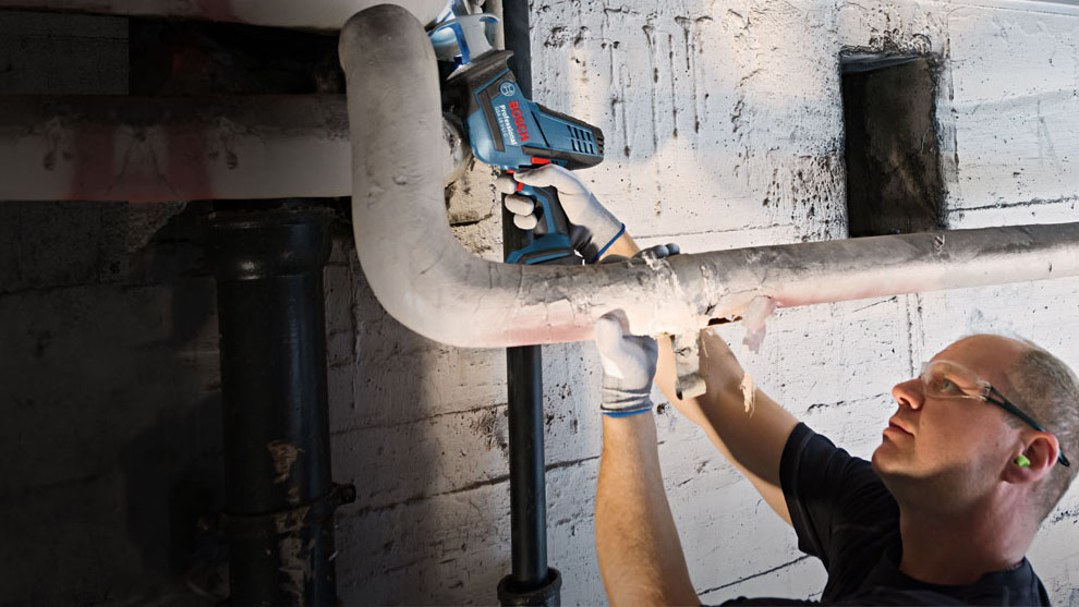 A craftsman is working with a blue Bosch Professional tool on pipes.