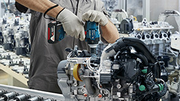 A worker wearing a helmet and protective mask is using a drill on scaffolding.