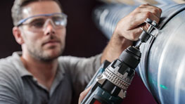 A craftsman wearing safety glasses operates a black Bosch drill.