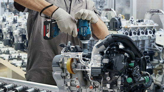 A worker wearing a helmet and mask is using a Bosch Professional tool.