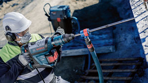 A worker with a helmet is using a Bosch Professional drill on a wall.