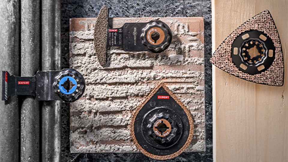 Three Bosch Expert tools on a rough surface with pipes.