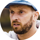 A bearded man is wearing a blue hat and looking serious.