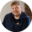 A smiling man with short hair is wearing a blue sweater.