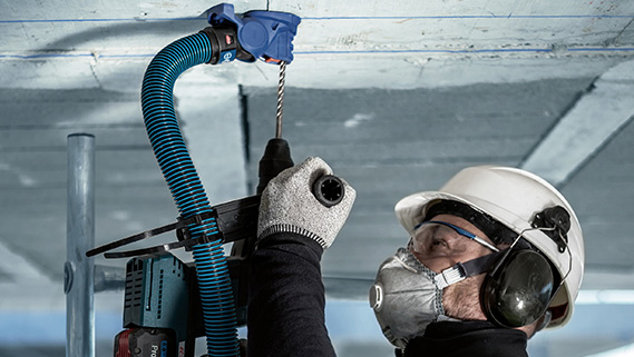 A craftsman wearing a helmet and hearing protection is drilling in the ceiling.