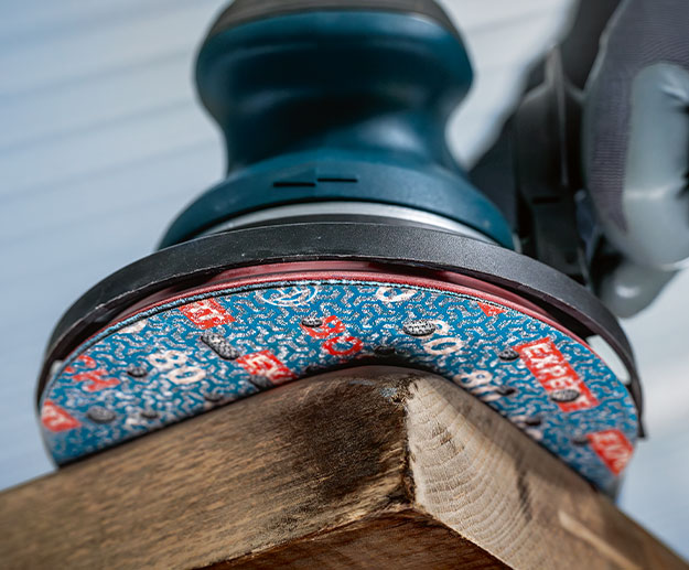 A Bosch Professional eccentric sander is standing on a wooden board.
