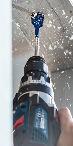 A Bosch Professional cordless drill with a blue drill crown is penetrating a ceiling.