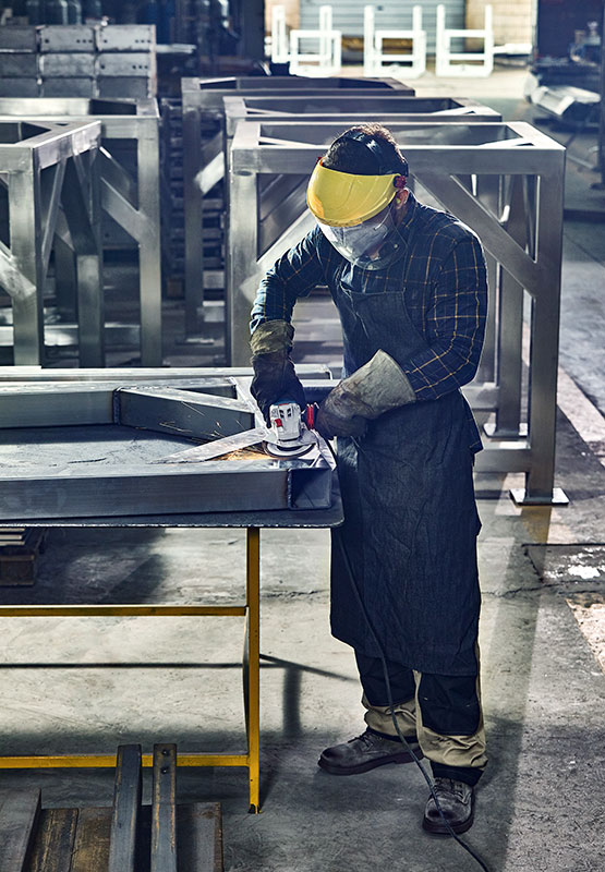 A worker wearing a safety helmet is grinding metal at a table in a workshop.