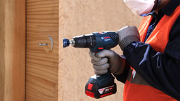 A man in an orange vest is using a Bosch cordless screwdriver.
