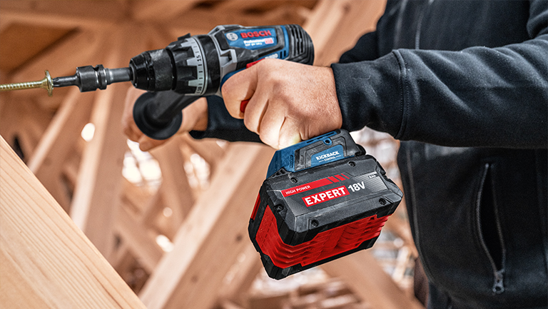 +28 Bosch Professional cordless screwdriver with red 18V battery in wood texture.