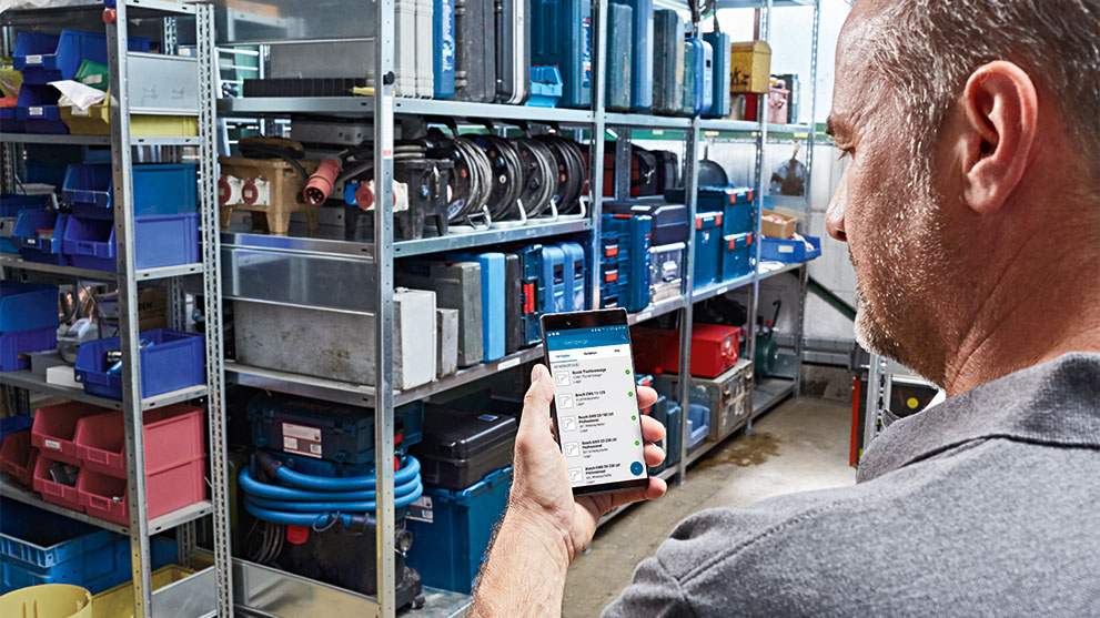 A man is looking at a smartphone in a tool storage.